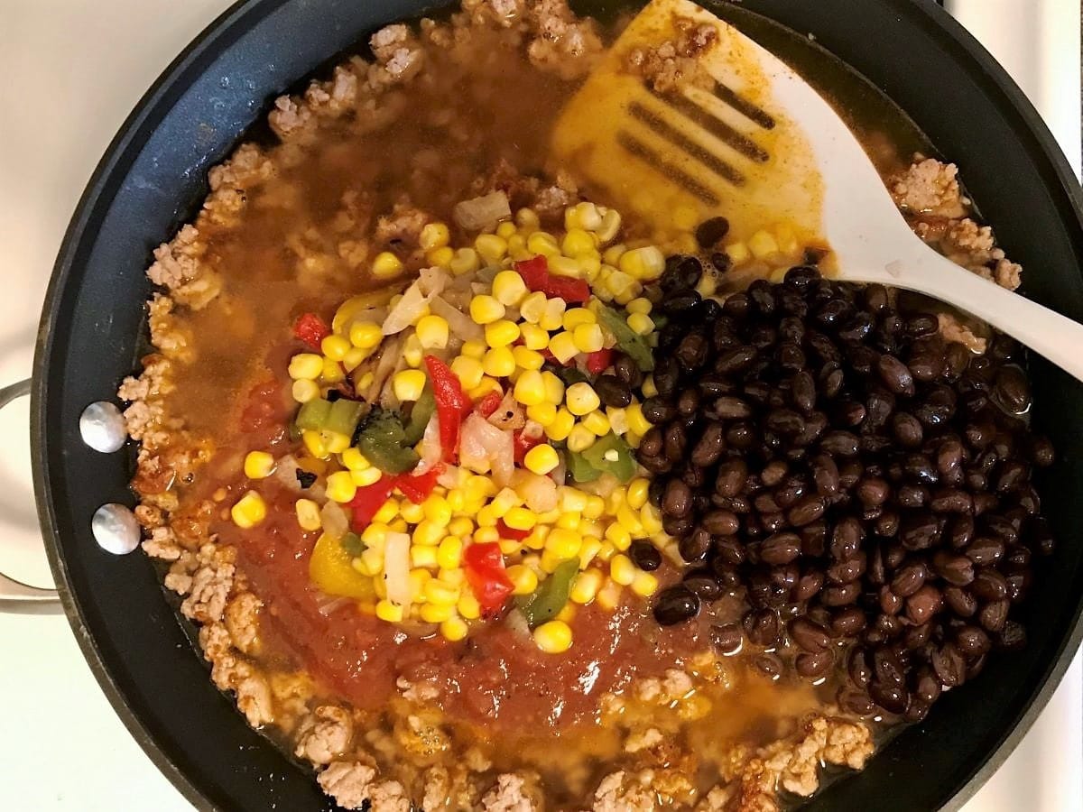 cooking turkey taco skillet, with corn, bell peppers, salsa, and black beans in a skillet
