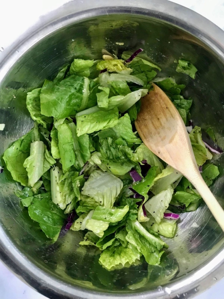 romaine lettuce in a metal bowl with a wooden spoon