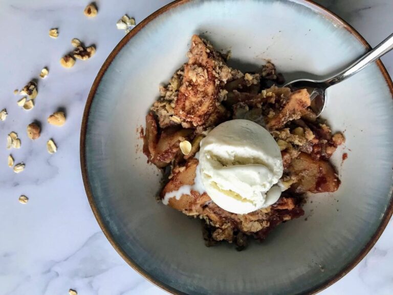 bowl of maple walnut apple crisp with vanilla ice cream on top.