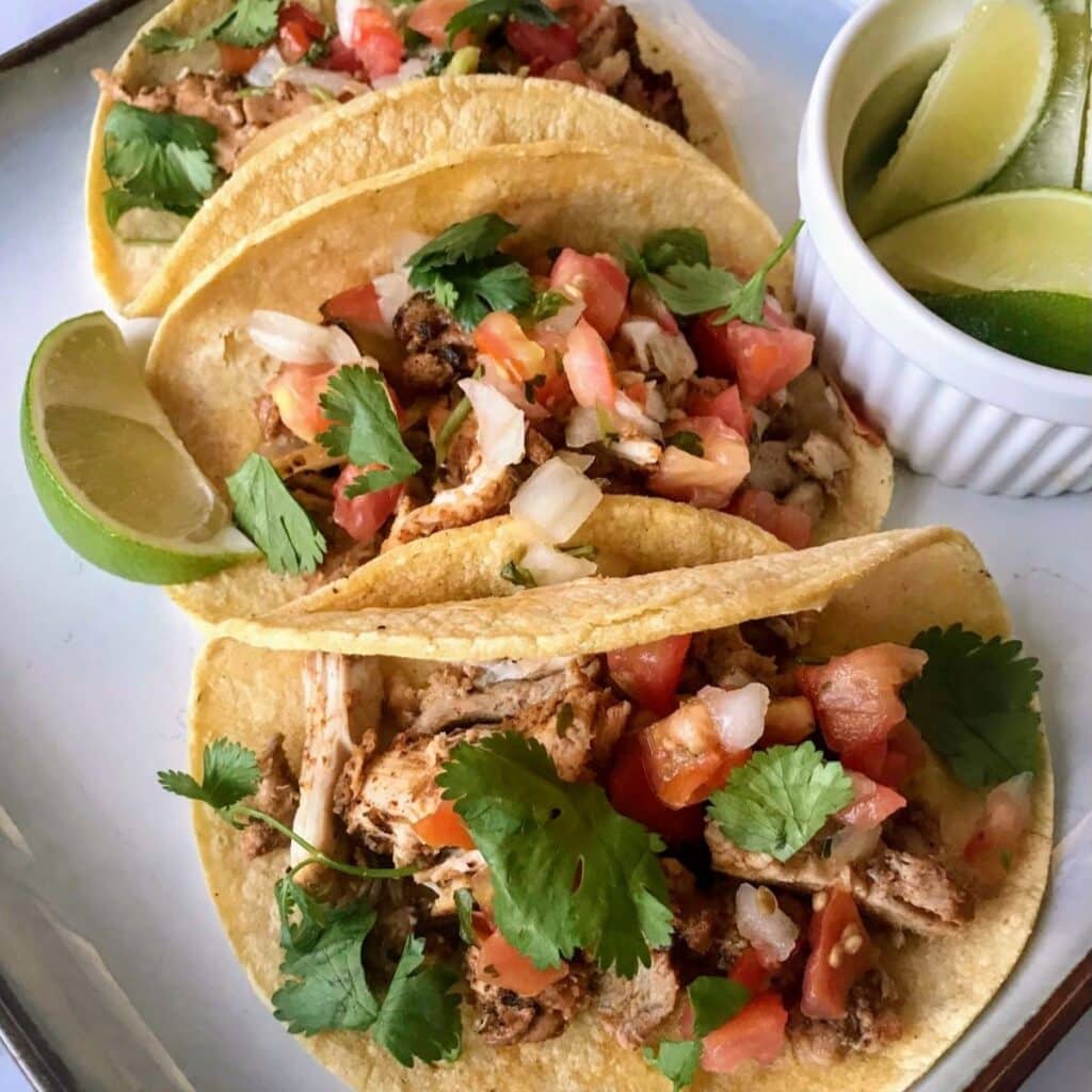 3 pollo asado tacos with a side of sliced limes.